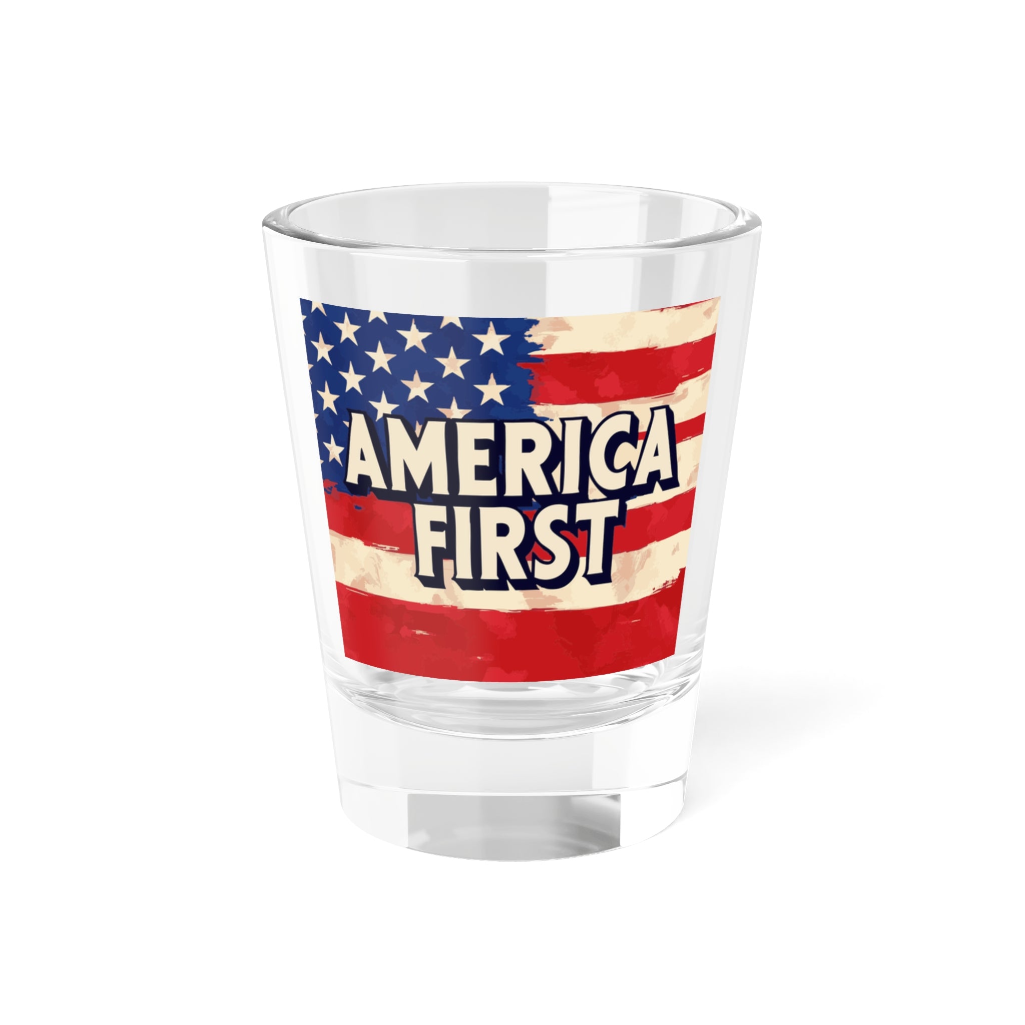 A clear glass shot glass with a patriotic design featuring the American flag and the text 'AMERICA FIRST' displayed on the front.