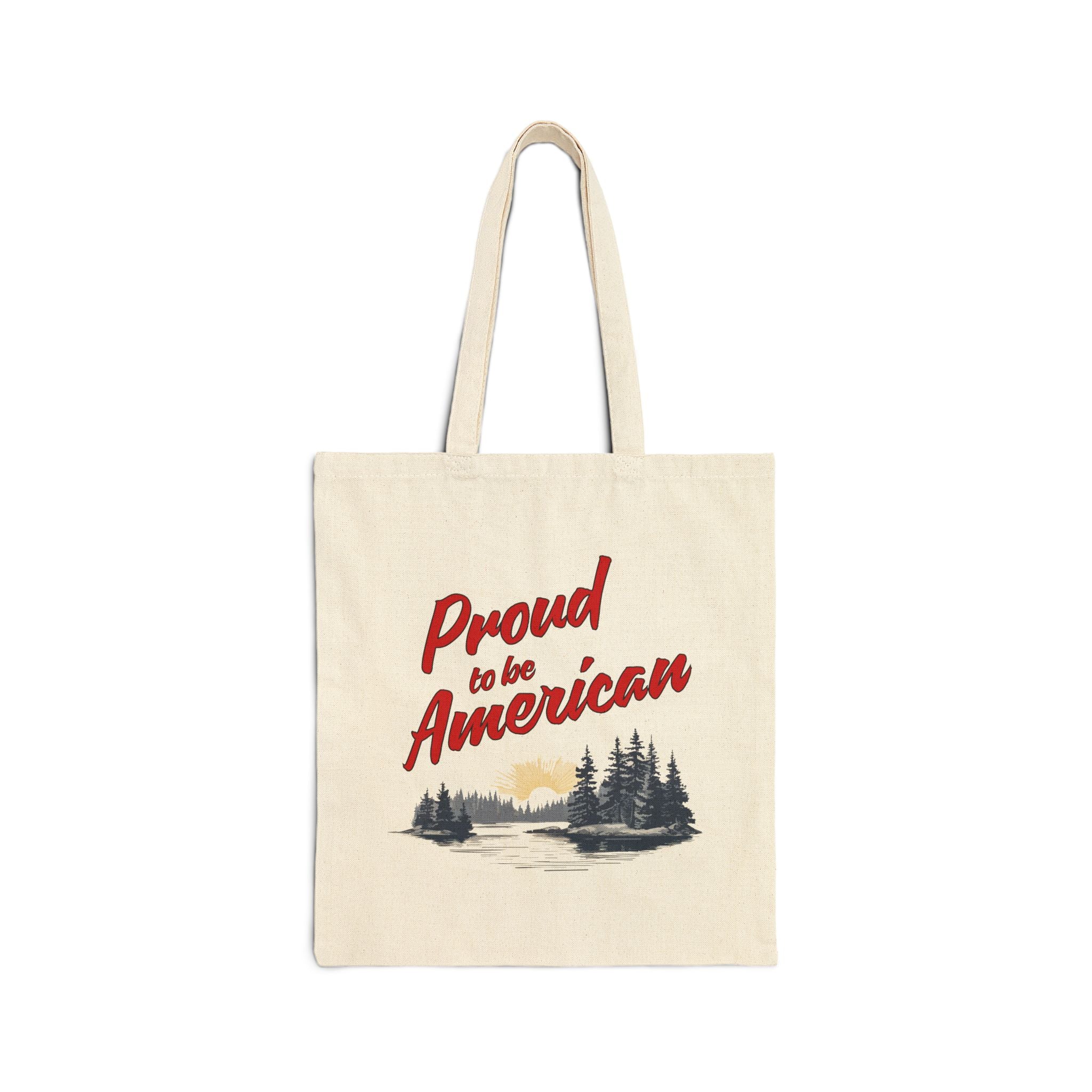 A beige cotton canvas tote bag with 'Proud to be American' printed in red text on the front, featuring a small illustration of a pine forest.